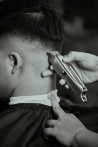 Detailed black and white close-up of a barber trimming a man's hair with clippers.
