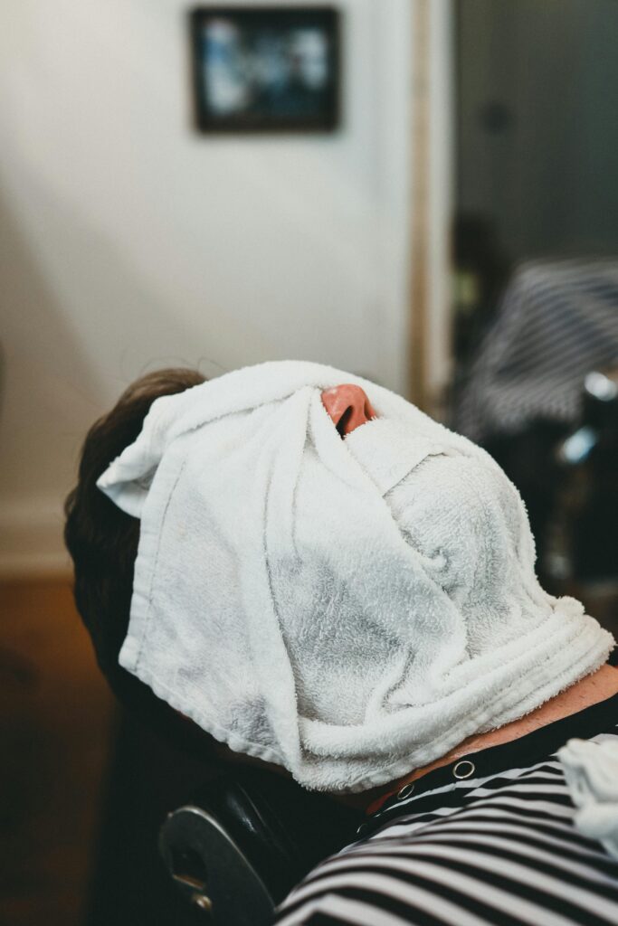 A man receives a relaxing hot towel treatment at a spa, emphasizing relaxation and self-care.