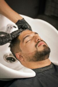 A man with closed eyes enjoys a calming hair wash at a barbershop sink.